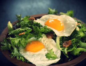 Two sunny side up eggs in a salad of greens with pecan garnishes