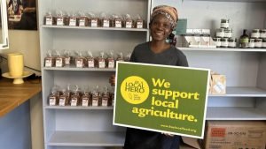 Woman in a store standing in front of shelves with farm products holding a green sign that says "We support local agriculture"